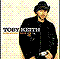 Pixelated static image of a person in black clothing against a light background with scattered dots, featuring visible text on the chest and partial text to the left.