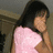 Pixelated image of a person with long dark hair wearing a light pink sleeveless top, positioned against a muted brown and gray background.