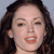 A pixelated close-up of a person with dark brown hair, light skin, and red lips, mouth open showing teeth, against a light gray background.
