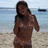 A pixelated static image shows a person standing on a beach with water and a distant object in the background.