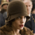 A pixelated image shows a person with light brown hair wearing a large dark brown hat, with a blurred background of indistinct figures.