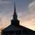 Silhouetted building with a tall spire against a gradient sky transitioning from light orange to dark blue.