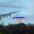 Pixelated static image showing a light blue sky with dark green foliage below and a rectangular structure in the center.
