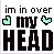 Pixelated text 'im in over my HEAD' with two heart icons above 'my', one green and one blue, on white background.