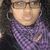 A person with curly dark hair wears glasses, a purple patterned scarf, and large hoop earrings in three showing slight head movement