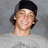 A pixelated image of a person wearing a black cap and gray shirt against a gray background, with vertical blue text on the right side.
