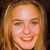 A pixelated close-up of a person with light brown hair, green eyes, and a broad smile showing teeth, set against a dark background.