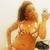 Woman in orange bikini taking selfie with smartphone, hand on hip, background with dark object.