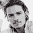 Static grayscale pixelated image of a person's face with dark hair, visible eyes, nose, mouth, and neck against a light background.