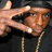 A person wearing a black hoodie and gold chain makes a hand gesture with fingers forming a frame around their face, visible