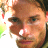 A pixelated close-up of a person's face with brown hair, visible eyes, nose, mouth, and beard stubble against a white background.