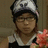 Pixelated image of a person wearing a black and white cap with dark brim, holding pink flowers against brown background.