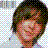 Pixelated close-up of a person's face with dark hair, visible eyes and nose, against a checkered background.