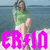 A person in a green shirt and white shorts sits on a beach with water behind them, overlaid by large pink text.