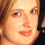 Pixelated close-up of a person's face with light brown hair, showing eyes, nose, mouth, and part of the neck against a dark background.