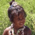A pixelated figure with dark hair wears a silver crown-like object on their head, standing against a green pixelated background.