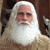 Static pixelated image of a person with long white hair and beard, wearing light-colored clothing against a dark brown background.