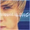 Close-up of a person's face with light brown hair and blue eyes, overlaid with semi-transparent text reading 'trapped in this' and a small white wing-like symbol.