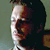 Pixelated static image of a person's face in profile view with visible facial features and partial clothing, set against a muted background.