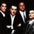 Four pixelated figures in white bow ties and dark suits against a black background, each with distinct facial features.