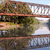 Static pixelated image of a bridge with greenery and water reflection under a light blue sky.