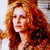 A pixelated portrait of a person with long red hair, wearing a dark top, against a light background with subtle color gradients.