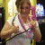 Pixelated image of a person with brown hair wearing a white sleeveless top and pink straps, holding an object near their chest against a bright background.
