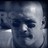 Pixelated grayscale image of a bald figure with dark eye patches and a faint smile, set against a dark background with light reflections.