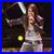 A pixelated figure in a light dress holds a microphone against dark and blue backgrounds with visible stage lighting.