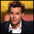 Static pixelated image of a person with brown hair wearing a white shirt and dark jacket against a yellow background.