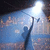 A pixelated figure in dark clothing raises one arm toward a bright light source against a blue-toned background with scattered lighter pixels.