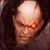 Pixelated close-up of a bald character's face with one glowing red eye, dark hair on sides, and brown-toned skin against a dark background.