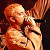 A pixelated contact sheet showing two frames of an animated icon featuring a cartoon character singing into a microphone on the left and green text reading "Original Icons .com" on the right against a dark background.