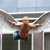 A pixelated figure with outstretched arms hangs from a metal railing against a blurred background of concrete and sky.