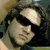 A pixelated image of a person with long dark hair and a black headband, wearing a light-colored shirt, with green text overlay reading '<3 Bam Margera' on the right side.