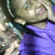 A person with light brown hair wearing a purple shirt, smiling and holding an object near their face in a pixelated image.