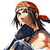 Pixelated image of a person with long brown hair tied back, wearing a dark sleeveless top and holding a microphone.