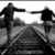 Two silhouetted figures stand on a road with one figure extending an arm toward the other against a bright background.