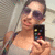 A pixelated image shows a person holding a small device with colorful squares, wearing a light-colored top and dark straps, against a blurred background.