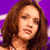 Pixelated close-up of a person with long brown hair against a purple background, showing partial facial features and a light-colored garment.