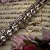 A silver flute with visible keys rests on a textured surface with pink and green fabric elements.