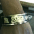 A pixelated static image shows a partial view of a character with brown hair and dark clothing, featuring a metallic belt buckle with indistinct symbols.