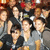 Group of pixelated figures in dark and light clothing with varied hair colors, some holding objects, against a blurred background.