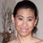 A person with dark hair pulled back, wearing earrings and a strapless top, smiling against a light background with blurred foliage.