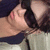 A person with dark hair and sunglasses lies on a light-colored surface, wearing a dark blue top, with subtle shifts in head position across frames.