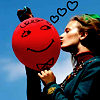 A person in a blue jacket kisses a red balloon with a smiley face, while three black heart outlines float above against a blue sky.