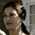 Pixelated close-up of a person with dark hair styled in an updo, wearing a light-colored top against a blurred background.