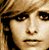 Pixelated close-up of a person's face with light brown hair, dark eyes, and neutral expression against blurred background.