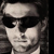 Pixelated grayscale image of a person wearing dark sunglasses and a light-colored headband, with a neutral expression and dark hair visible on the sides.