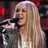A static image shows a person with long blonde hair holding a microphone against a bright pink background with purple text.